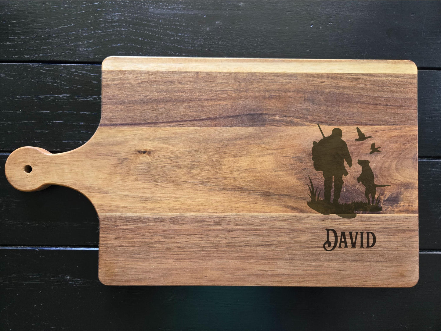 Wooden cutting board with engraved design and name 'David' on a dark wooden surface