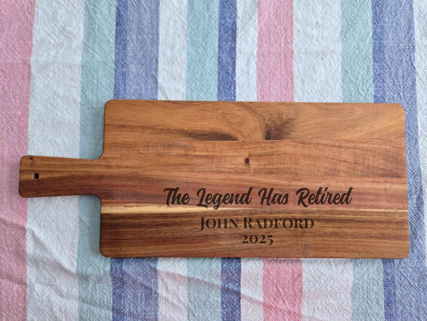 Wooden cutting board with engraved text on a striped fabric background